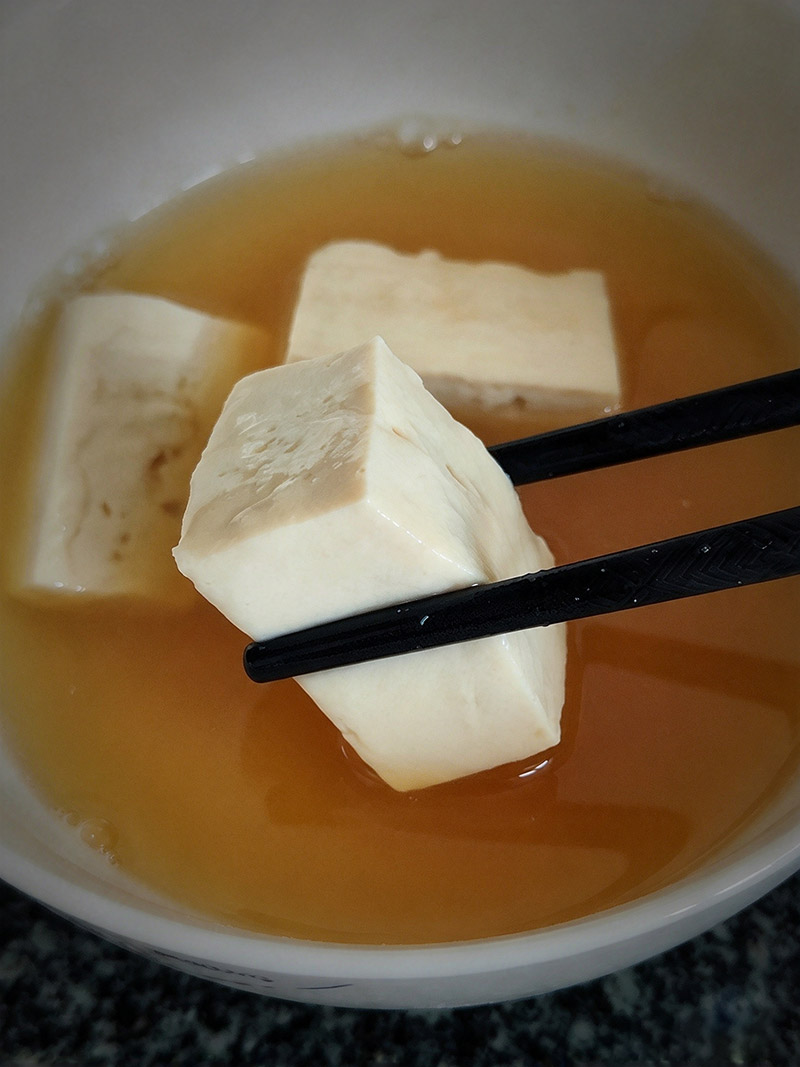 Dipping a steamed firm tofu cube into a bowl of fermented bean curd culture liquid