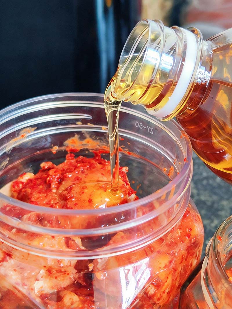 Pouring cooked and cooled vegetable oil over spice-coated hairy tofu in a glass jar
